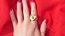 Load image into Gallery viewer, Hand wearing a dainty thrills gold ring with a heart-shaped gem on a red fabric background
