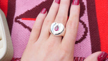 Load image into Gallery viewer, Hand wearing a dainty thrills silver ring with a red ruby gemstone against a pink and red patterned background that says Menstruation Matters Belfast Scarf