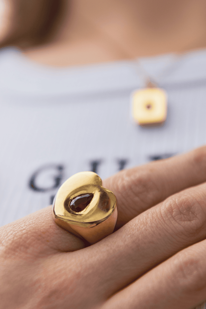 Gold dainty thrills ring with a red gemstone worn on a finger, with a blurred background.