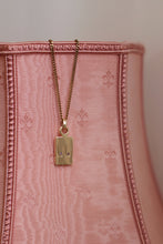 Load image into Gallery viewer, A gold-plated pendant necklace with a chain, attached to a pink textured surface.

