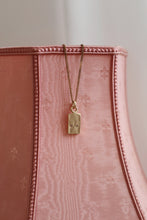 Load image into Gallery viewer, A gold-plated pendant necklace with a chain, attached to a pink textured surface.
