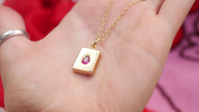 Load image into Gallery viewer, Dainty Thrills gold necklace with a dainty pendant featuring a red gemstone held in a hand against a red background.
